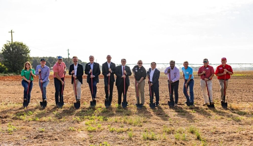 A group of people pose with shovels in an agricultural field during a ground breaking ceremony.